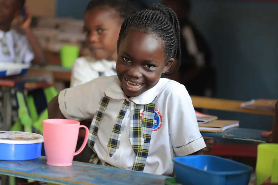 A smiling pupil at her desk with her lunch bowl and mug
