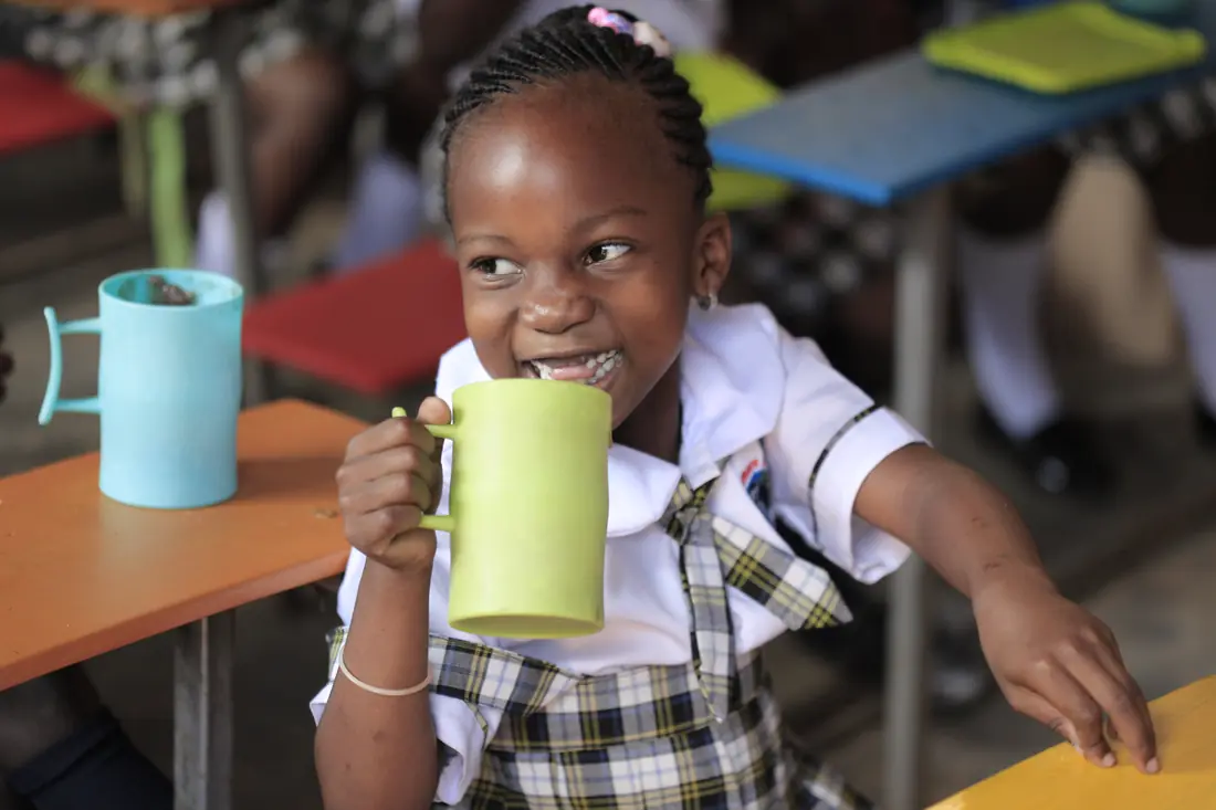 A pupil drinks safe water from a mug at her desk in class